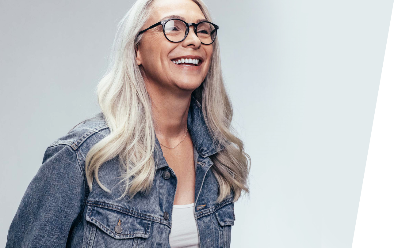 Confident, youthful woman with shiny white hair and stylish black-framed glasses looks off into the distance and smiles.